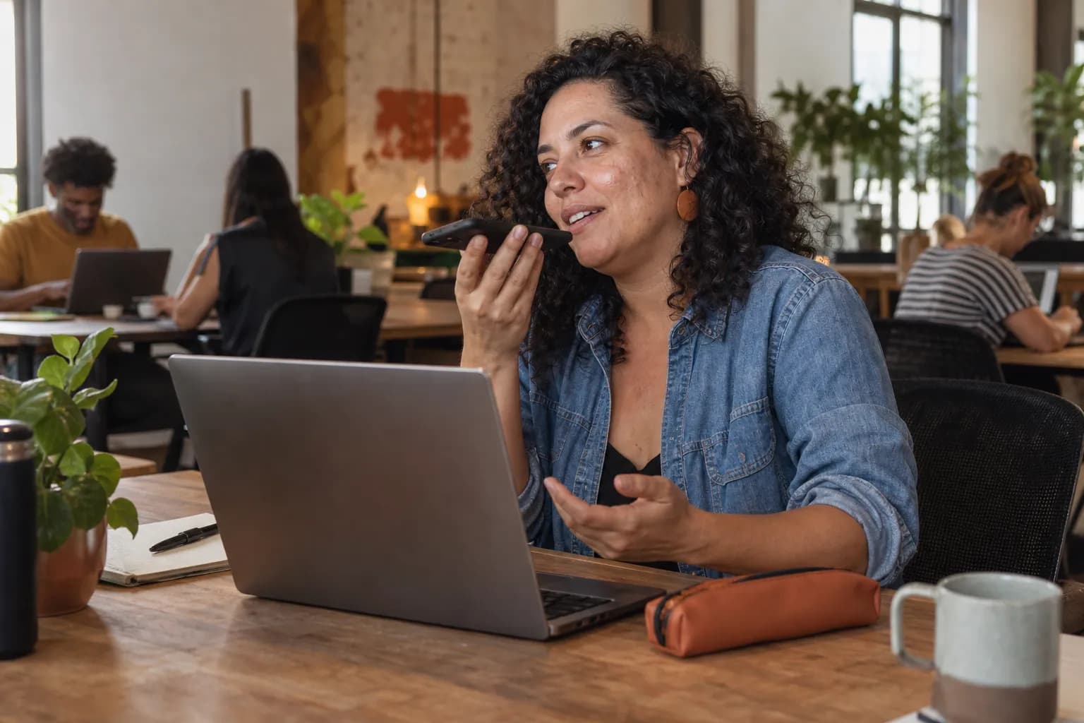 Profissional autônoma grava um áudio no celular numa mesa de coworking, recomendando algo que usa no trabalho.