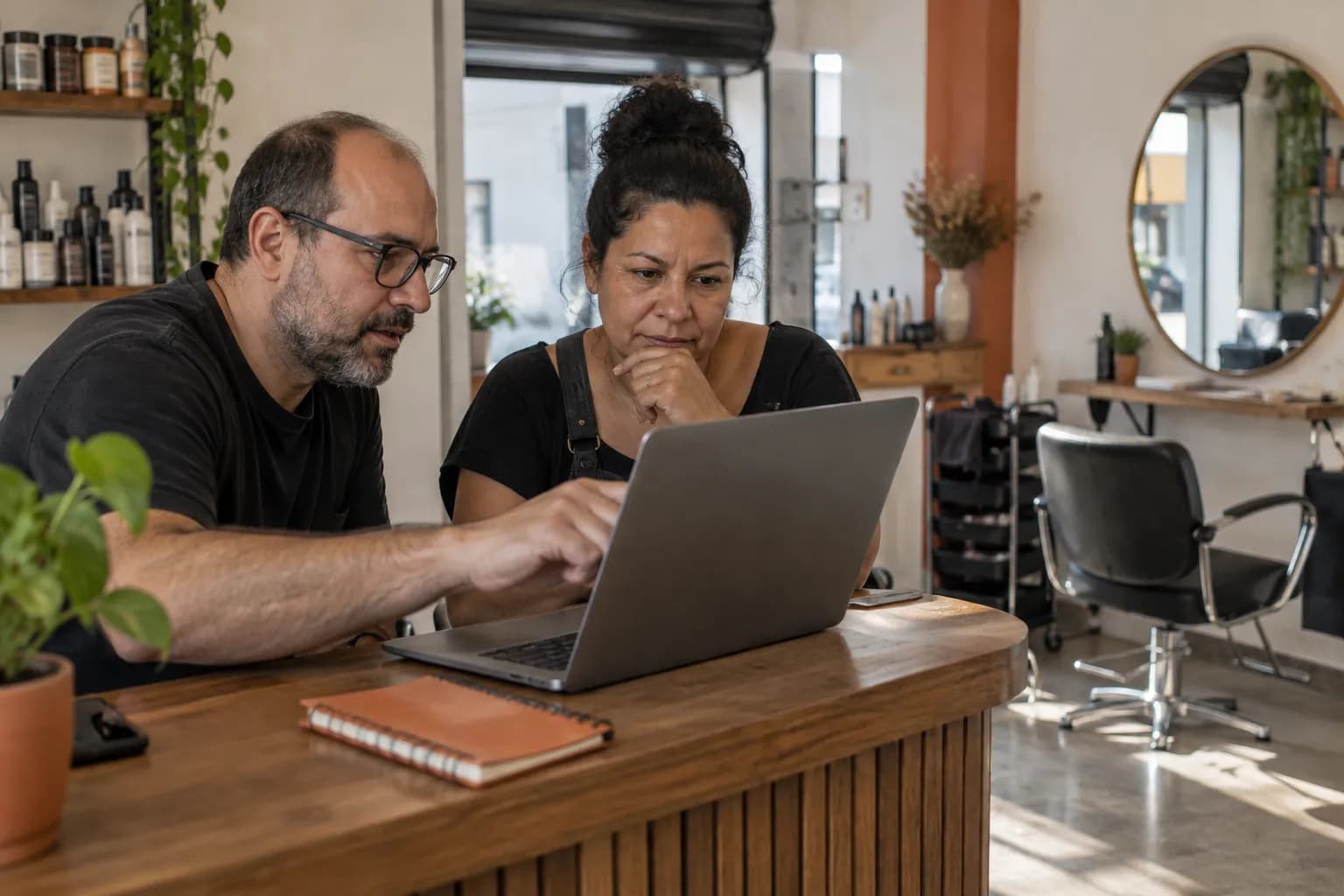 Consultor de agência mostra algo no notebook para a dona de um salão, no balcão da recepção antes de abrir.